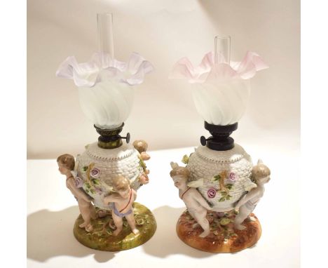 Pair of late 19th century Continental porcelain oil lamps, the lamp reservoirs supported by three cherubs on circular bases w
