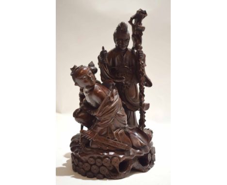 Large Chinese wooden carving of a couple, the man holding a staff, the lady with a sword standing against a jardiniere with l