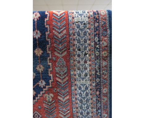 TWO RUGS the indigo and light pink ground with central panel with stylised floral heads with a conforming border a wine and g