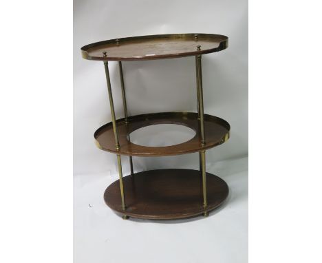 A MAHOGANY AND BRASS FRAMED THREE TIER SIDE TABLE of oval outline with raised gallery on tubular column supports with brass b