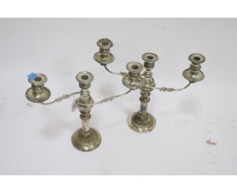 A PAIR OF GEORGIAN STYLE SILVER PLATED CANDLE STICKS the central column issuing scrolled arms with foliate embossed drip pans