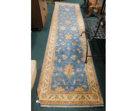 A COTTON RUNNER the light blue ground with central floral panel within a beige border with conforming decoration 303cm x 82cm