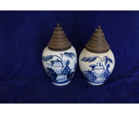 A pair of Dutch Delft tobacco jars with stepped metal covers, the first with blue and white body depicting a gentleman smokin