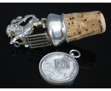 A white metal bottle stopper modelled as a rampant lion, together with a silver cricket medallion. (2) 