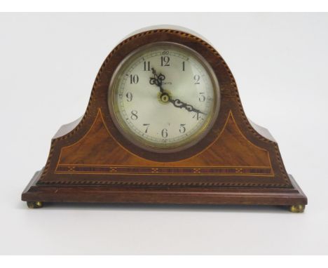 An Edwardian mahogany and chequered strung mantel clock of arched outline with 8cm silvered Arabic dial,  raised on squat bun