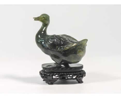 A 20th century spinach jade figure of a duck, carved standing with its head turned to one side, the mottled stone with some p