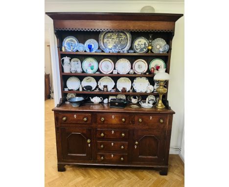 A Georgian oak two part dresser with a shelf upper section and a base with six drawers and two cupboards with brass knob hand