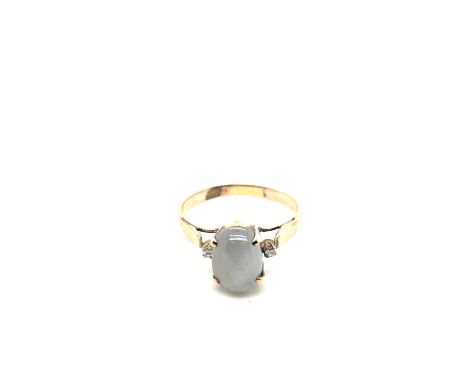 An oval cabochon star sapphire gemstone ring flanked with two round brilliant cut diamonds. Unhallmarked, assessed as 9ct gol