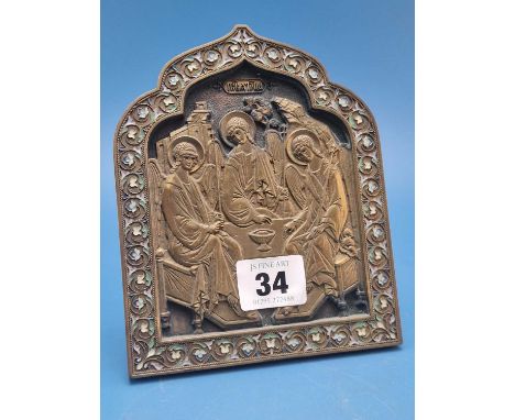 An easel backed bronze icon depicting three angels seated holding staffs around a table bearing a footed bowl all within a cl