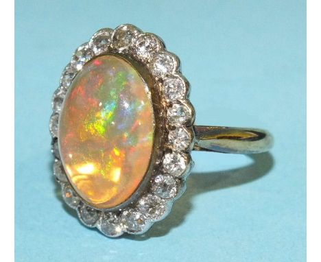 A fire opal and diamond cluster ring, the oval opal, approximately 15 x 12 x 6mm collet set within a surround of twenty old b