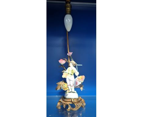 A CONTINENTAL BRASS TABLE LAMP, decorated with a central French ceramic figure surrounded by large ceramic flower heads