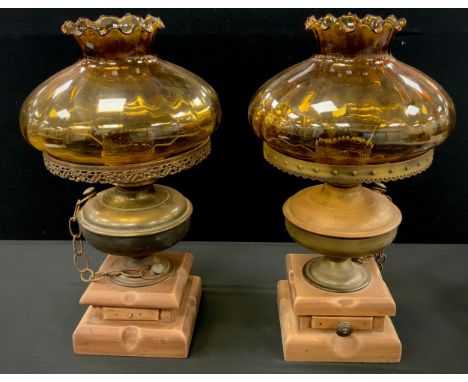 A pair of oil lamp table lamps, later converted to electricity/candles,  amber glass shades, brass reservoirs, wooden plinth,