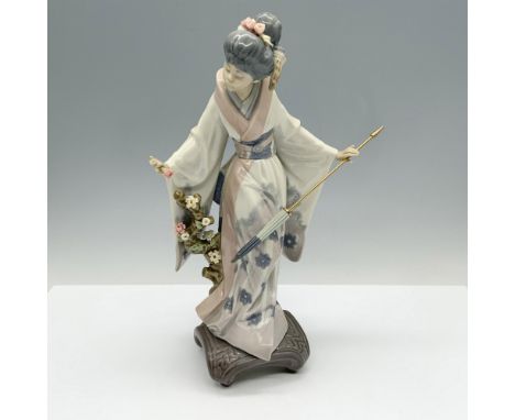 Beautiful figure of a woman modeling a floral decorated kimono as she holds a parasol and stands alongside a branch with flow