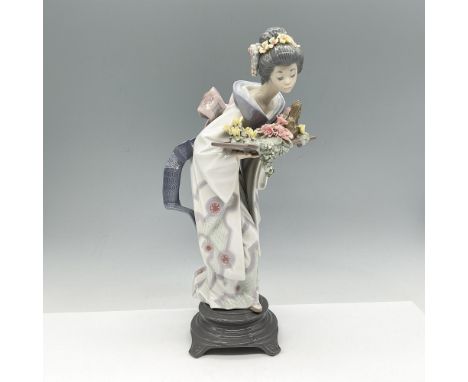 Delicate Japanese figure of young woman wearing kimono holding a tray of colorful flowers. Prominent colors are yellow, blue,