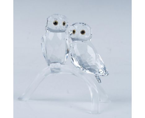 Two adorable owls perch side by side on a tree branch, their piercing yellow eyes shining brightly. Swarovski backstamp. This