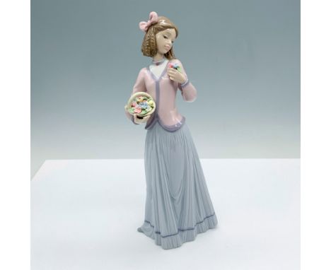 A woman elegantly dressed in a pink blouse and lavender skirt gracefully holds a basket of flowers in one hand and a bouquet 
