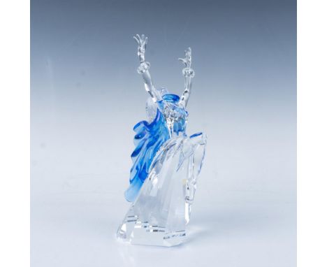 A woman dancer in a flowing dress adorned with blue accents gracefully kicks one knee in the air while raising her hands high