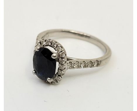 A platinum, diamond and sapphire ring,&nbsp;claw set mixed oval cut sapphire to centre bordered by oval ring of numerous pave