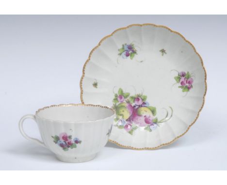 A Worcester fluted teacup and saucer, painted in a distinctive palette with sprays of 'Spotted Fruit' and sprigs of flowers, 