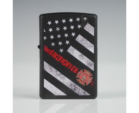 Zippo matte black lighter featuring a distressed American flag design accented with "FIREFIGHTER" in bold red lettering along