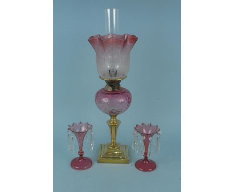 A Victorian brass oil lamp with cranberry glass reservoir and etched cranberry shade plus a pair of cranberry glass lustre's 