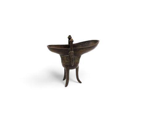 An 18th century bronze tripod ritual wine vessel or jue, of conventional form with a mask loop handle to one side and stnadin
