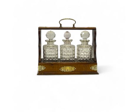 A late 19th century three bottle oak tantalus, with silver plated mounts and containing three cut glass decanters  31cm high 