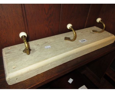 Set of three gilt brass and ceramic coat hooks on a lime waxed backboard
