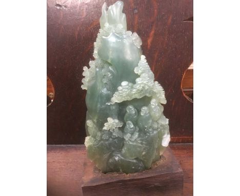 A carved jade on green hardstone mountain scene with Buddhas, 19cm high on hardwood stand
