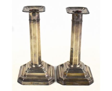 A pair of George V loaded hallmarked silver candlesticks, each raised on stepped square sectioned base with presentation insc