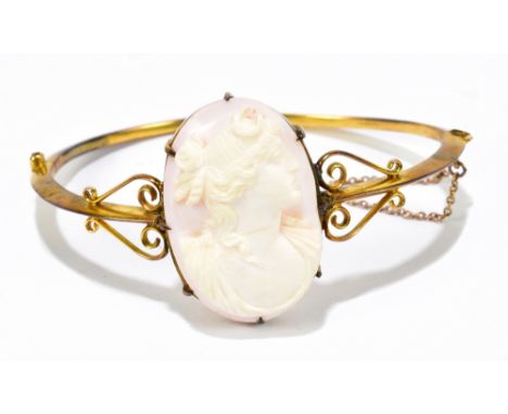 An Edwardian yellow metal hinged snap bangle with large oval cameo plaque within an openwork frame, interior width 62mm, appr