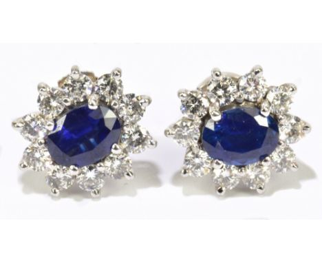 A pair of 18ct white gold sapphire and diamond cluster earrings, the oval sapphires four claw set within a border of ten roun