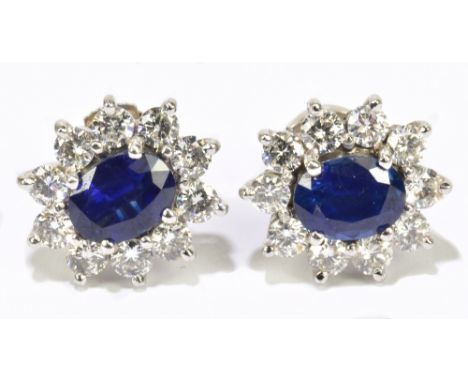 A pair of 18ct white gold sapphire and diamond cluster earrings, the oval sapphires four claw set within a border of ten roun