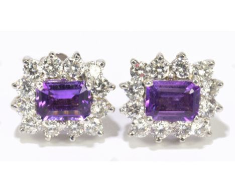 A pair of white metal amethyst and diamond ear studs, each with central emerald amethyst within a frame of twelve round brill