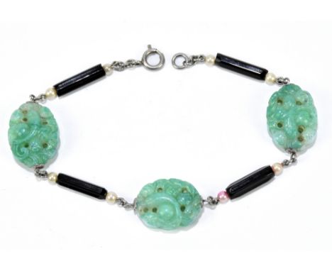 An Art Deco bracelet set with three carved jade panels inset between seed pearls and black hexagonal shaped spacers, with pla