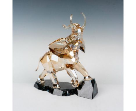 A beautiful sand colored crystal elephant raising its head and trunk to the sky while walking over a granite base. Swarovski 