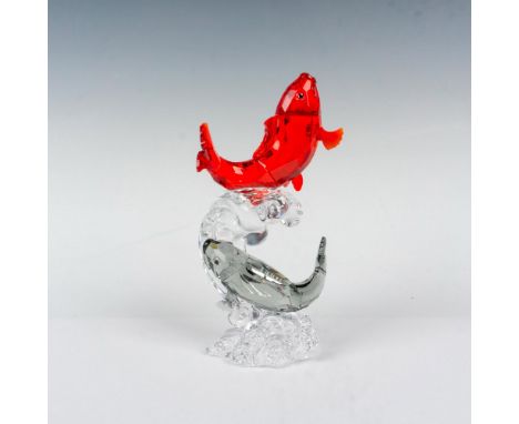 A beautiful crystal figurine of two fish, one a deep red color, the other a light charcoal color swimming on top of a clear c