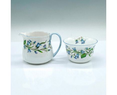 A set of white creamer and sugar bowl adorned with blue flower pattern and light blue trims. Shelley backstamps. Creamer: 4"L