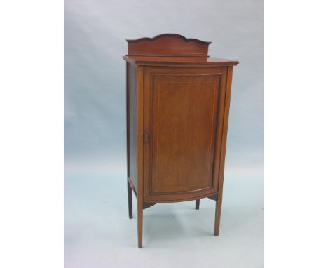 An Edwardian inlaid mahogany music cupboard, bow-fronted panelled door enclosing three shelves, 1ft. 9in.