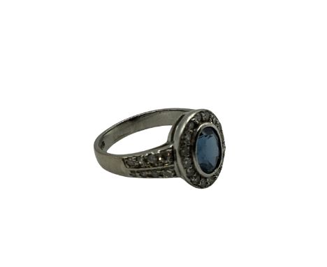 A 18ct white gold sapphire and diamond ring, central oval free cut sapphire in a rub over setting with a surround of 16 singl