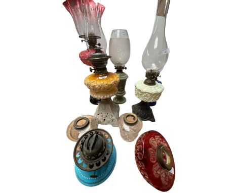 A collection of five oil lamps one with opaline reservoir and cast metal base, the largest with etched cranberry glass shade 