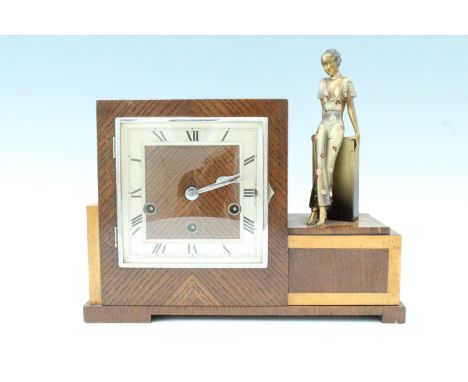 A 1950s Moderne oak cased figural mantle clock, having a three train movement striking and chiming on gongs, the square case 