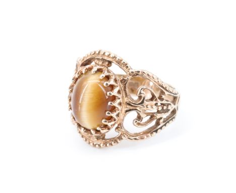 A 1970s 9 ct gold tiger's eye ring, having a 7.5 x 9.5 mm oval tiger's eye cabochon set on broad shoulders of cast openwork b