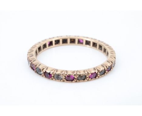 A spinel, white garnet and yellow metal eternity ring, having 26 pave set stones, the settings accentuated by engraved sides 