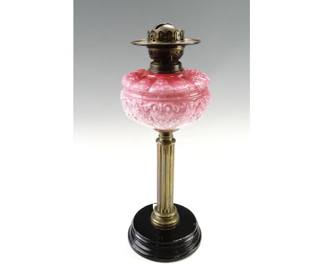 A late 19th Century columnar oil lamp, having a pink glass reservoir, on a tiered black-glazed base, 48 cm
