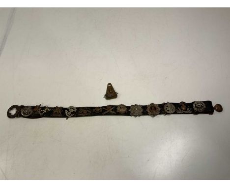 A WWI Naval leather belt mounted with fourteen regimental cap badges and one loose, including Cornwall Light Infantry, Somers