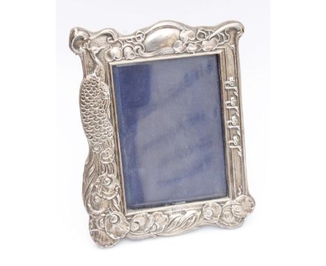 An Edwardian silver Art Nouveau photo frame, raised with peacock scrolls and flowerheads, of shaped outline with an easel bac