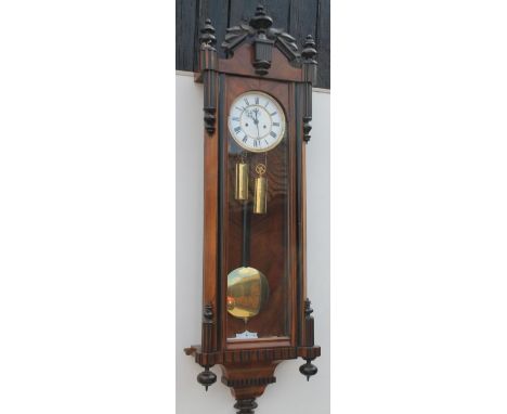A late 19th/early 20thC Vienna walnut and ebonised wall clock, with a shaped crest, turned finials and enamel dial with Roman
