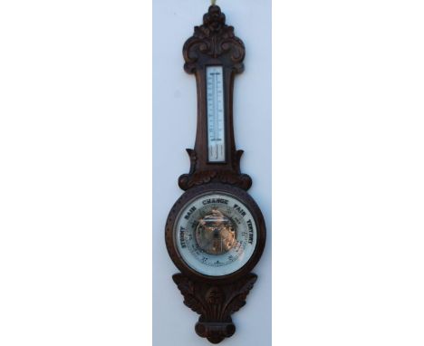 A Victorian aneroid barometer, in carved oak case, with opaque glass thermometer, the dial with ceramic insert, and printed d