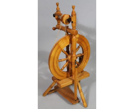A modern light wood spinning wheel, with central articulated cog, on shaped base set with foot pedal, 93cm high.